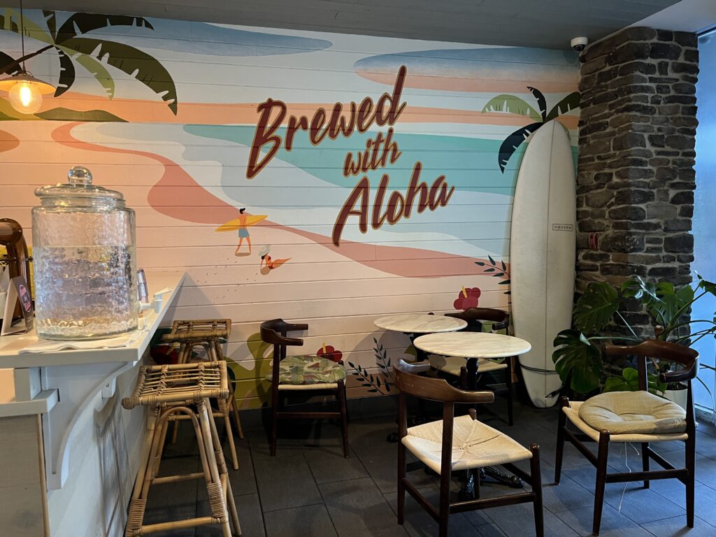 The wall at Honolulu Coffee - a vibrant mural with palm trees, a beach, and "Brewed With Aloha" written on it.