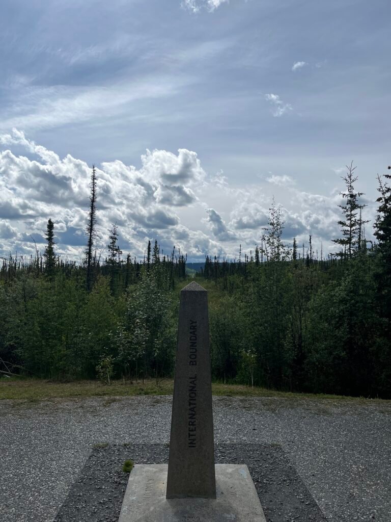 A border monument reading "INTERNATIONAL BOUNDARY" with a line cleared in the forest behind it