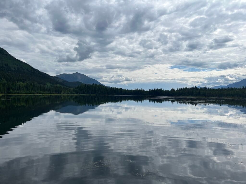 a still lake with mountains in the background and clouds
